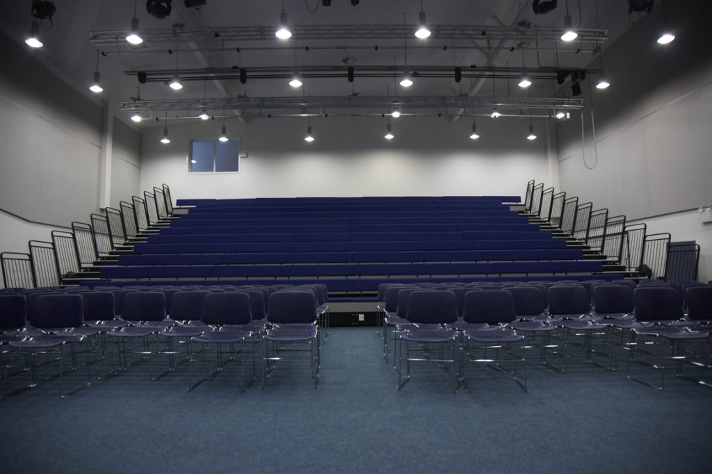 Photo of the main conference hall in Leigh Academy Longfield, featuring dark blue tiered seating.
