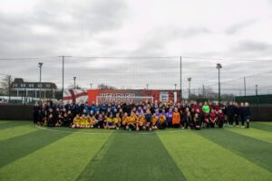 A large group of students in football kits, smiling in front of a goal